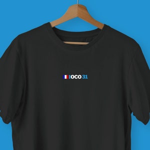 Może przedstawiać: Czarny T-shirt z małą haftowaną flagą Francji i tekstem "IOCO 31" w kolorze niebieskim.