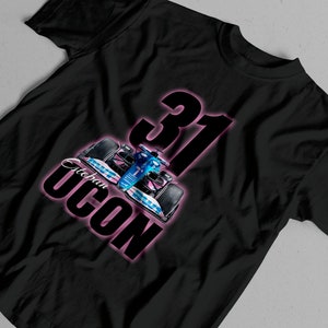 Może przedstawiać: Czarny T-shirt z różowym obramowaniem numeru 31 i nazwą Esteban Ocon. W środku projektu znajduje się niebieski i biały samochód wyścigowy.
