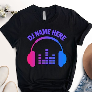 May include: Black t-shirt with a graphic of a pair of headphones with a sound equalizer and the text "DJ NAME HERE" in a gradient of pink and blue.