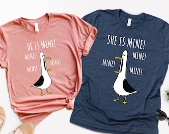 May include: Two t-shirts with a cartoon seagull graphic and the text "He is mine! Mine! Mine!" and "She is mine! Mine! Mine!" on a pink and blue background.