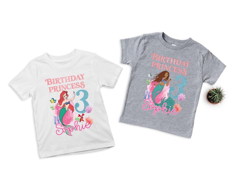 May include: Two short-sleeved t-shirts, one white and one gray, featuring a mermaid graphic. The white shirt has a red-haired mermaid design with the text "Birthday Princess 3 Sophie." The gray shirt has a brown-haired mermaid design with the same text.