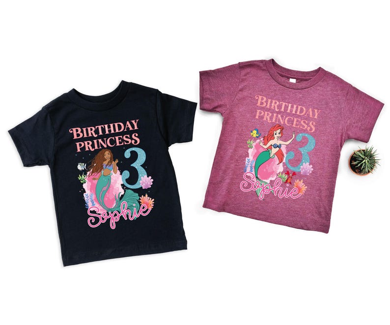 May include: Two short-sleeved t-shirts featuring mermaid graphics. One is navy blue, the other is maroon. Both shirts have the text "Birthday Princess" and a number 3, with a mermaid illustration and a name.