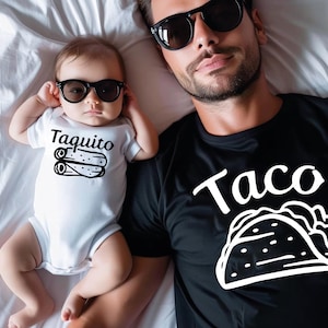 May include: A father and son wearing matching shirts. The father's shirt is black with the word "Taco" and a white outline of a taco. The son's shirt is white with the word "Taquito" and a white outline of a small taco.