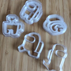 May include: Set of six clear plastic cookie cutters shaped like the characters from the video game Among Us. The cutters are stacked on top of each other.