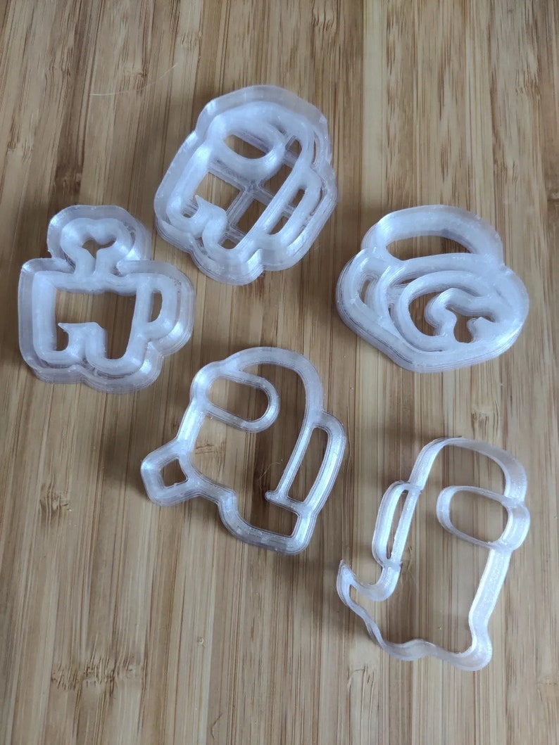 May include: Set of six clear plastic cookie cutters shaped like the characters from the video game Among Us. The cutters are stacked on top of each other.