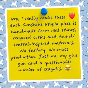 May include: A bright yellow square note pinned with a blue thumbtack, featuring dark blue handwritten text: Yep, I really make these. Each Sunshine Utopia piece is handmade from real stones, recycled corks and found/coastal-inspired materials.