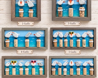 May include: Six framed wall art pieces featuring pebble seagulls perched on wine corks against a painted blue ocean background. The sets display between two and seven birds, some wearing colourful plastic sunglasses, all mounted in rustic wooden frames.