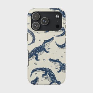 May include: A cream-colored smartphone case featuring a repeating pattern of dark blue illustrated alligators in various poses. The case has a black camera module cutout at the top with three circular lenses and a small flash component.