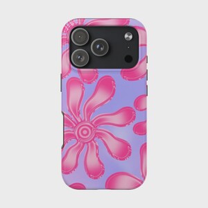 Puede incluir: Funda de teléfono con un patrón repetido de flores rosas sobre un fondo lila claro. Las flores tienen un efecto degradado, pasando del rosa oscuro al rosa claro. La funda tiene un módulo de cámara negro.
