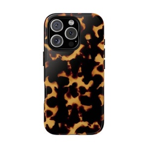 Puede incluir: Una funda de teléfono negra con un patrón de caparazón de tortuga. La funda tiene una protuberancia de cámara elevada con tres lentes.