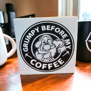 May include: White wooden sign with a black and white illustration of a cartoon dwarf with a pickaxe. The sign reads "Grumpy Before My Coffee".