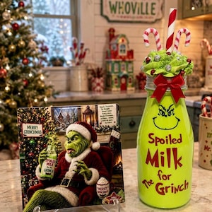 Puede incluir: Un letrero cuadrado con un personaje Grinch vestido de Santa Claus y una botella de vidrio verde lima con un lazo rojo, una pajita de bastón de caramelo y nata montada artificial verde. La botella tiene el texto "Spoiled Milk for The Grinch".