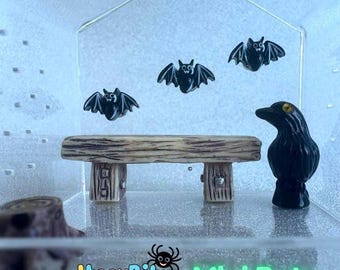 May include: Miniature Halloween-themed scene featuring three black bats, a wooden bench, and a black crow figurine. The scene is set inside a clear acrylic box. The text "ItssyBitssy Mini Bats Spider" is at the bottom.