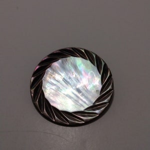 May include: A round, iridescent mother-of-pearl button with a carved black border.