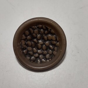 May include: A brown button with a textured surface that resembles small stones.