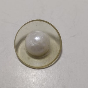 Peut inclure: Un bouton en plastique transparent avec un centre de perle blanche.