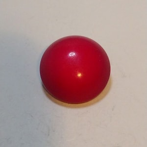 Puede incluir: Un botón redondo de color rojo brillante.