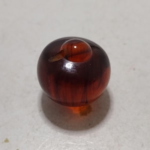 May include: A dark brown glass button with a smaller, round, clear glass top.