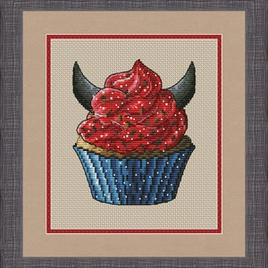 Può includere: Un cupcake rosso e blu con corna da diavolo e codette rosse. Il cupcake è in un pirottino di carta blu e bianco.