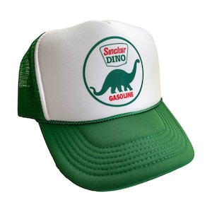 May include: White trucker hat with a green mesh back. The front of the hat features a circular logo with a green dinosaur and the text "Sinclair Dino Gasoline".