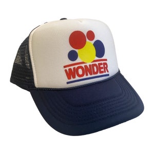 May include: A white and blue trucker hat with a red, yellow, and blue Wonder Bread logo. The logo features a cluster of colorful circles and the word "Wonder" in red letters.
