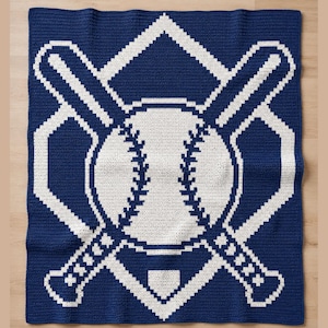 May include: A rectangular crochet blanket featuring a dark blue background with a large white graphic design. The pattern displays a central baseball with visible stitching, crossed baseball bats, and a home plate shape outlined in white yarn.