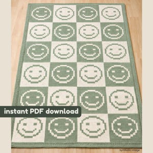 May include: A crocheted rug featuring a checkerboard design of smiling faces in white and sage green. The rug has a sage green border. The text "instant PDF download" is visible in the lower left corner.