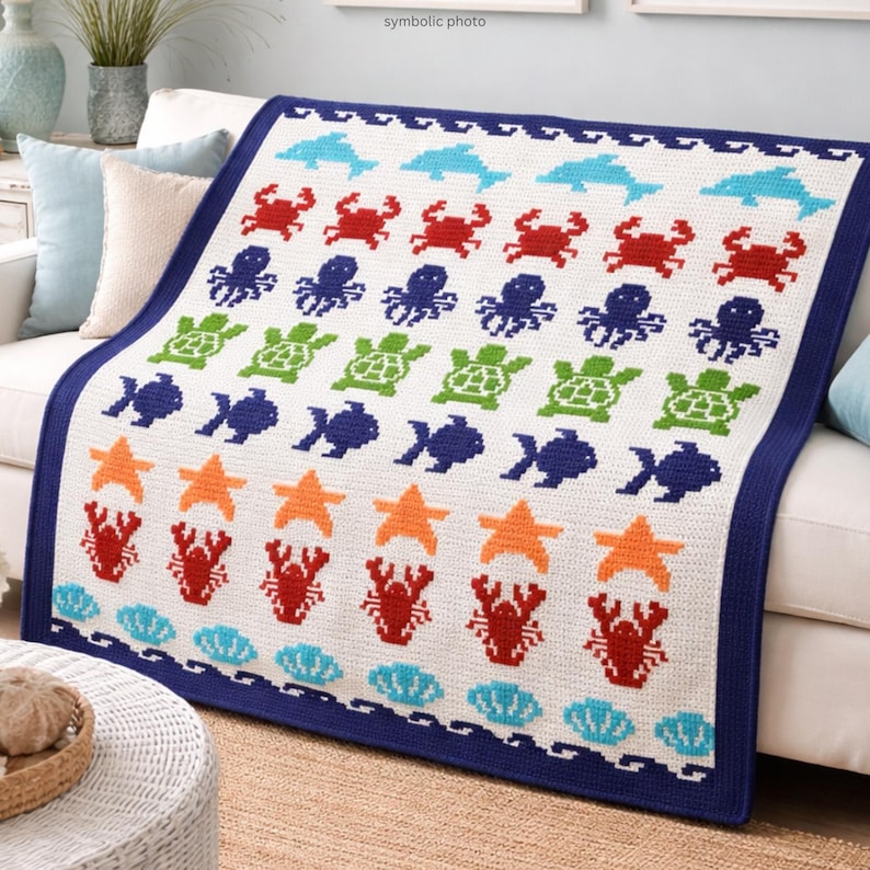 May include: A white crocheted blanket with a navy blue border, featuring a repeating pattern of sea creatures. The design includes dolphins, crabs, octopuses, turtles, fish, starfish, lobsters, and seashells in various colors.