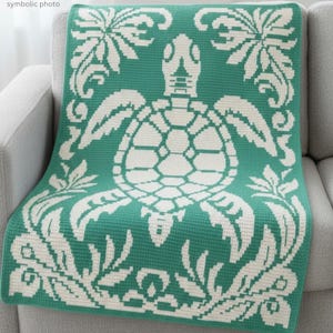 May include: A teal and white throw blanket featuring a sea turtle design. The blanket is draped over a gray sofa. The turtle is in the center, surrounded by floral and scrollwork patterns. The blanket is made of a soft, textured material.