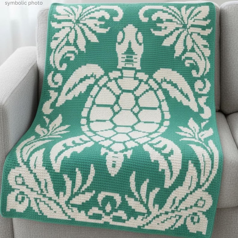 May include: A teal and white throw blanket featuring a sea turtle design. The blanket is draped over a gray sofa. The turtle is in the center, surrounded by floral and scrollwork patterns. The blanket is made of a soft, textured material.