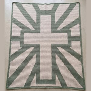 May include: A square, handmade crochet blanket featuring a large cross design. The cross and radiating lines are sage green, set against a cream-colored background. The blanket has a sage green border.