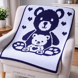 Könnte beinhalten: Eine weiß-marineblaue gehäkelte Babydecke mit einem Teddybären-Design. Die Decke zeigt einen großen Bären mit einem kleineren Bären im Inneren, umgeben von Herzen. Sie hat einen marineblauen Rand. Der Text "SYMBOLIC IMAGE" steht unten.
