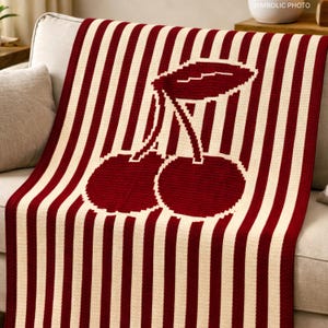 Puede incluir: Una manta a rayas rojas y crema con un diseño de cerezas. La manta presenta un patrón de rayas verticales crema y un gran gráfico de cerezas en el centro. Las cerezas son rojas con un contorno y tallo blancos.