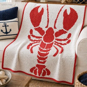 Könnte beinhalten: Eine weiße Decke mit einem großen roten Hummer-Design. Die Decke hat einen roten Rand und ist über ein weißes Sofa drapiert. Dekorative Kissen mit nautischen Motiven sind sichtbar.