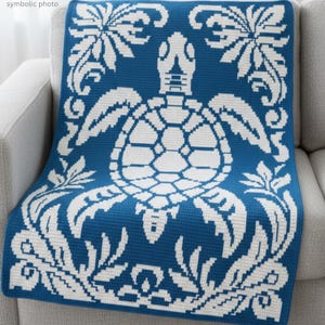 May include: A blue and white throw blanket featuring a turtle design. The blanket has a large turtle in the center, surrounded by floral and leaf patterns. The blanket is draped over a gray sofa.