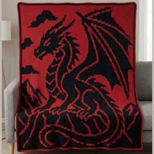 May include: A crocheted blanket featuring a black dragon design against a red background. The dragon is detailed with wings, a long tail, and a fierce expression. The blanket is draped over a gray sofa, showcasing the intricate craftsmanship.