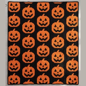 May include: A rectangular blanket featuring a repeating pattern of orange jack-o'-lanterns on a solid black background. Each pumpkin is rendered in a pixelated style with triangular eyes and a jagged mouth, arranged in a grid across the entire surface.