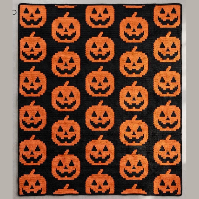 May include: A rectangular blanket featuring a repeating pattern of orange jack-o'-lanterns on a solid black background. Each pumpkin is rendered in a pixelated style with triangular eyes and a jagged mouth, arranged in a grid across the entire surface.