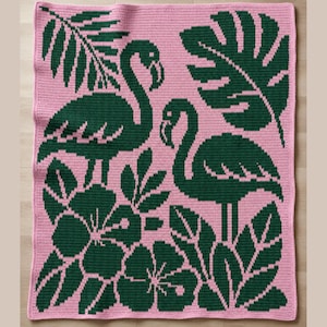 Puede incluir: Una manta rosa tejida a ganchillo con un diseño de flamenco y hojas tropicales de color verde oscuro. El diseño incluye dos flamencos, flores de hibisco y hojas grandes.