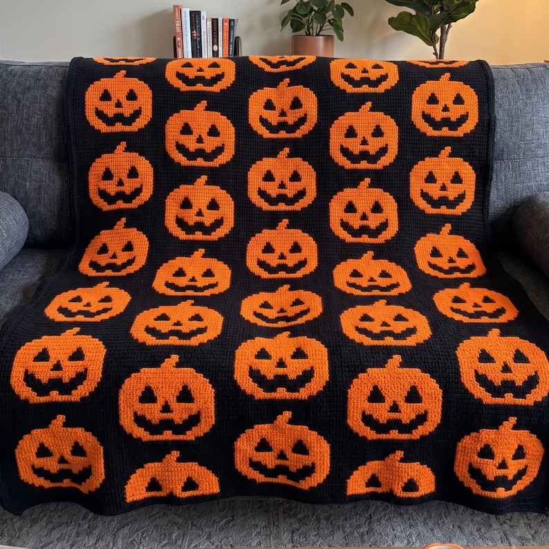 May include: A rectangular crochet blanket featuring a repeating pattern of orange jack-o'-lanterns against a solid black background. The design consists of multiple rows of pixelated pumpkin faces with triangular eyes and jagged mouths.