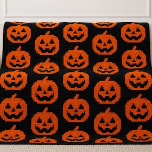 May include: A black crochet blanket featuring a repeating pattern of orange jack-o'-lanterns. The design consists of multiple rows of pumpkins with triangular eyes, noses, and jagged mouths arranged in a grid across the entire textile surface.