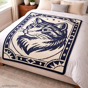 May include: A navy blue and cream-colored crocheted blanket featuring a large cat face design. The cat's face is in the center, surrounded by a decorative border with geometric shapes and stars. The blanket is displayed on a bed.