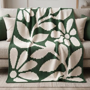 May include: A rectangular crochet blanket featuring a two-tone pattern of large, stylized white flowers and leaves set against a deep forest green background. The textile displays a consistent, dense stitch texture throughout the entire surface.