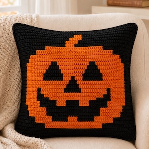 May include: A square crochet pillow cover featuring a pixelated jack-o'-lantern design. The pillow is primarily black with a large, centered orange pumpkin graphic. The pumpkin has black triangular eyes, a triangular nose, and a jagged mouth.