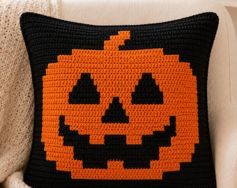 May include: A square crochet pillow cover featuring a pixelated jack-o'-lantern design. The pillow is primarily black with a large, centered orange pumpkin graphic. The pumpkin has black triangular eyes, a triangular nose, and a jagged mouth.