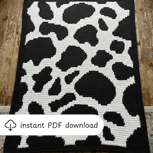 May include: A black and white crochet blanket with a cow print design. The blanket features large, irregular black spots on a white background. The blanket is rectangular and has a black border. The text "instant PDF download" is visible.