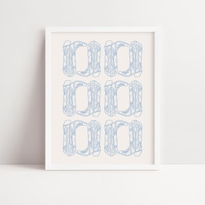 May include: A white framed print with a repeating pattern of blue cowboy boots. The boots are outlined in a light blue color and have a detailed design.