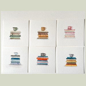 Può includere: Sei dipinti ad acquerello quadrati su carta ruvida, ognuno raffigurante una pila di libri sormontata da una tazza da tè. Le tazze variano per colore e motivo, includendo design verdi, marroni, rosa, blu, a righe bianche e nere e floreali.