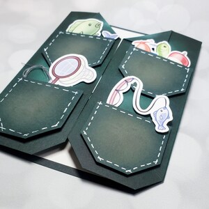 May include: A green card with a pocket design featuring various fishing-themed illustrations, including a fish, a net, and a fishing rod.
