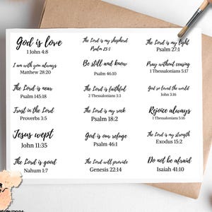 May include: A white card with black text featuring Bible verses. Verses include "God is love," "The Lord is my shepherd," and "Do not be afraid." The card is on a brown envelope, with a paintbrush and decorative elements in the background.